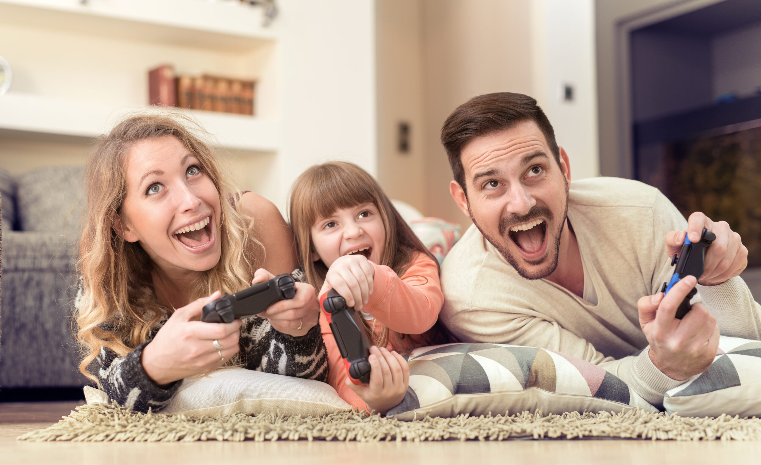 Young smiling couple playing video games in livingroom at home with daughter.